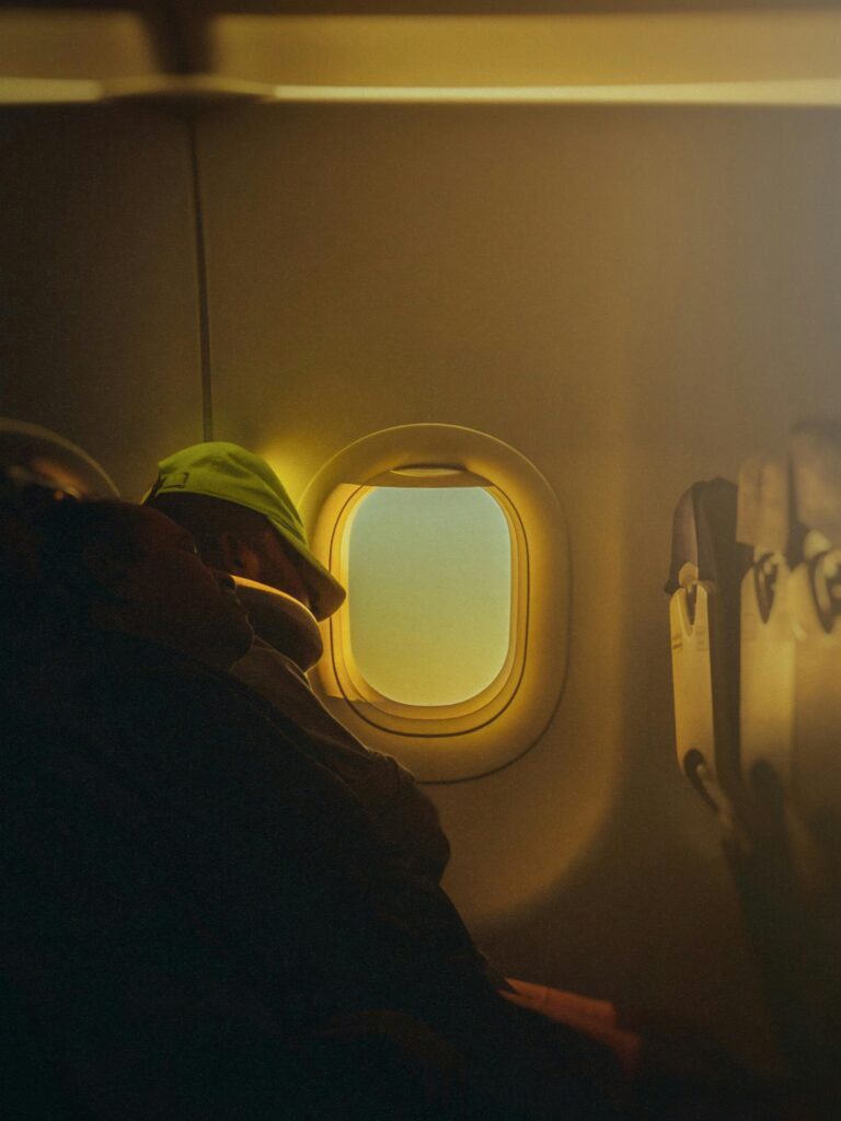 pexels-photo-14880761-14880761 A person rests peacefully by an airplane window, warm light filtering through.