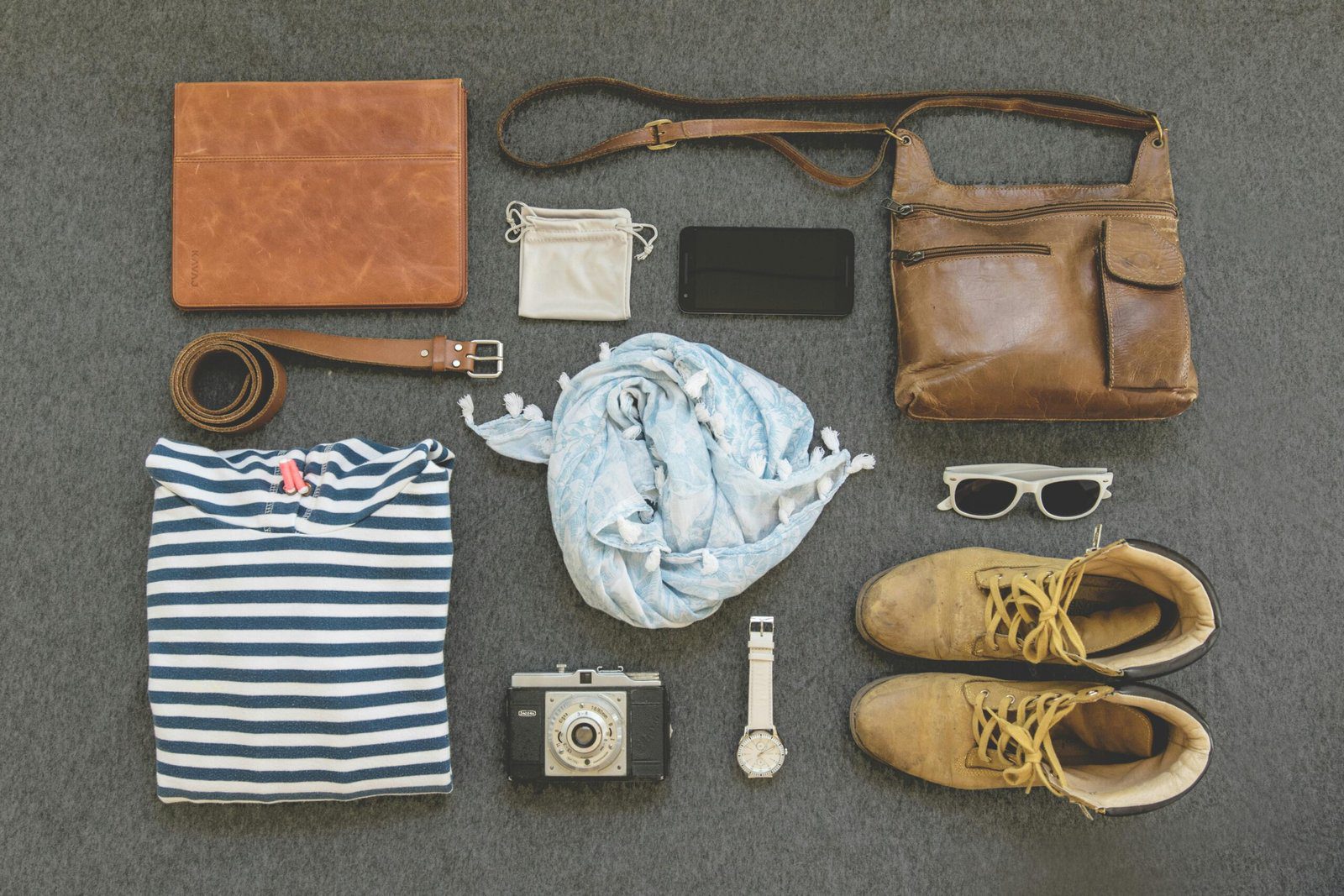 Vintage travel essentials flat lay with leather bags, shoes, camera, and clothing. What are the best travel accessories? This article will tell you and they might not be what you think.